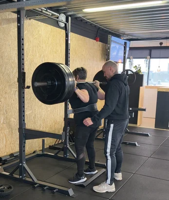 Personal trainer spot een klant tijdens een barbell back-squat bij Fit Up Leiderdorp